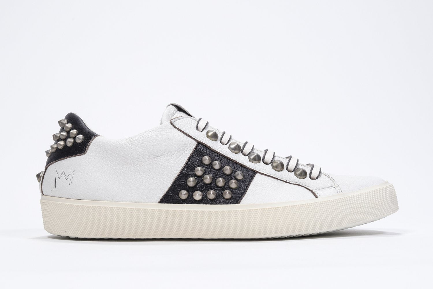 Side profile of low top white and black sneaker. Full leather upper with studs and vintage rubber sole.