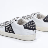 Three quarter back view of low top white and black sneaker. Full leather upper with studs and vintage rubber sole.