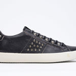 Side profile of low top black sneaker. Full leather upper with studs and vintage rubber sole.