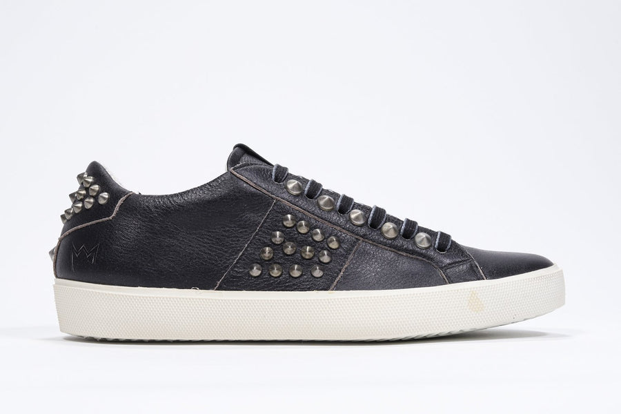 Side profile of low top black sneaker. Full leather upper with studs and vintage rubber sole.