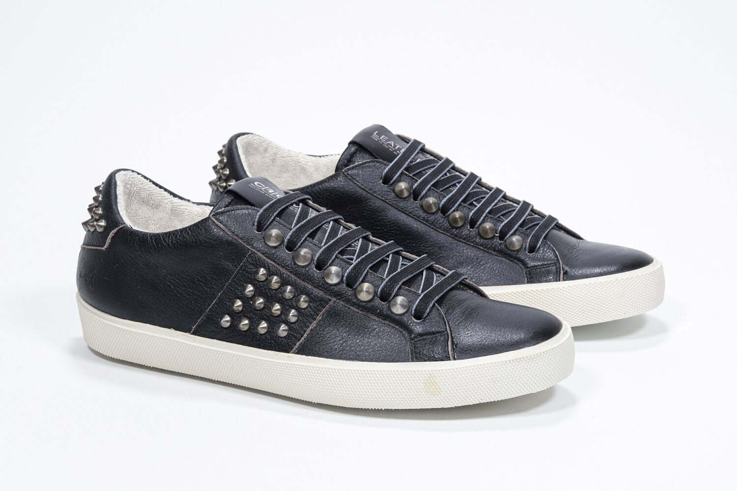 Three quarter front view of low top black sneaker. Full leather upper with studs and vintage rubber sole.
