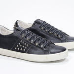 Three quarter front view of low top black sneaker. Full leather upper with studs and vintage rubber sole.