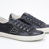 Three quarter front view of low top black sneaker. Full leather upper with studs and vintage rubber sole.