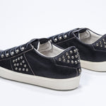 Three quarter back view of low top black sneaker. Full leather upper with studs and vintage rubber sole.