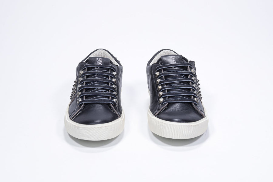 Front view of low top black sneaker. Full leather upper with studs and vintage rubber sole.