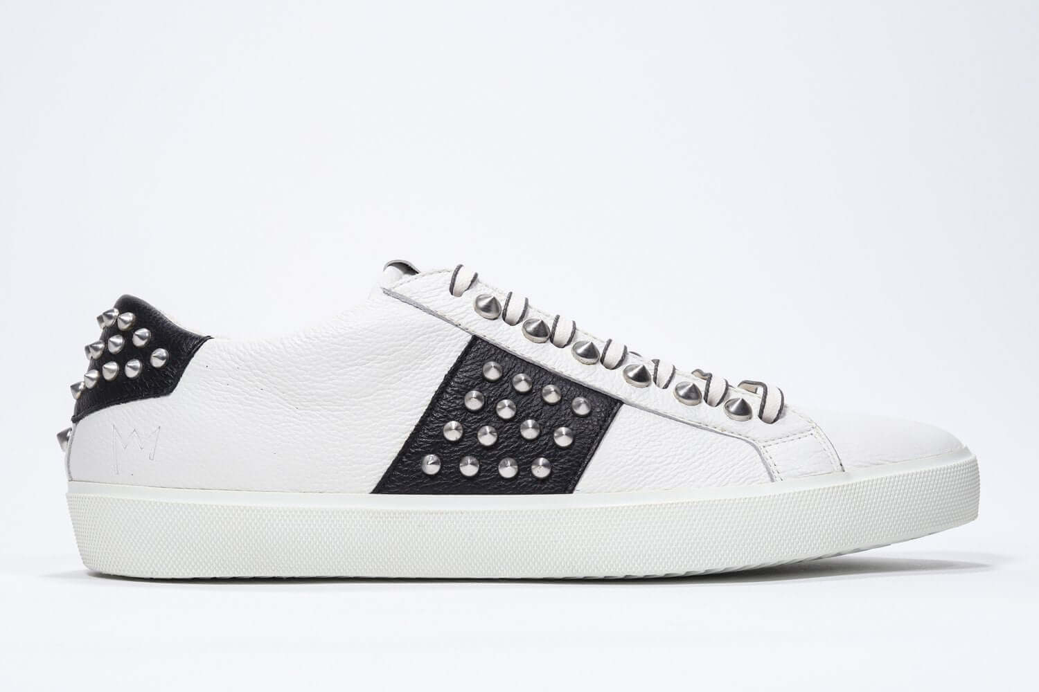 Side view of low top white and black sneaker. Full grain leather upper with silver studs and white rubber sole.