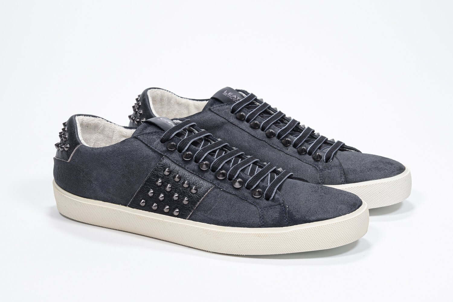 Three quarter front view of low top navy sneaker. Suede upper with gunmetal studs and vintage rubber sole.
