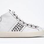 Side profile of mid top white sneaker. Full leather upper with studs, an internal zip and vintage rubber sole.