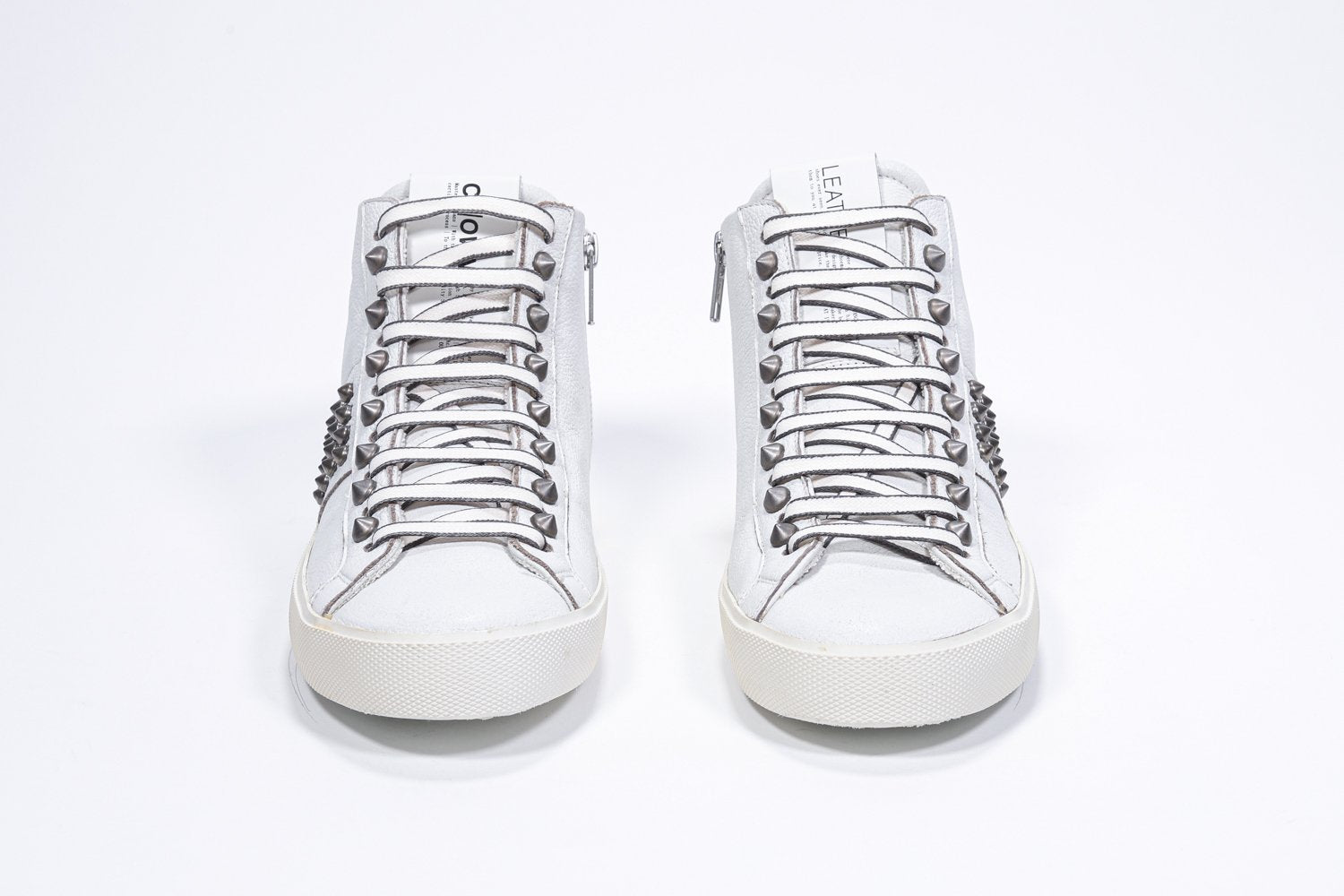 Vue de face d'une paire de chaussures blanches sneaker. Tige en cuir avec clous, fermeture à glissière intérieure et semelle en caoutchouc vintage.