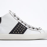 Profil latéral d'un mid top blanc et noir sneaker. Tige en cuir avec clous, fermeture à glissière interne et semelle en caoutchouc vintage.