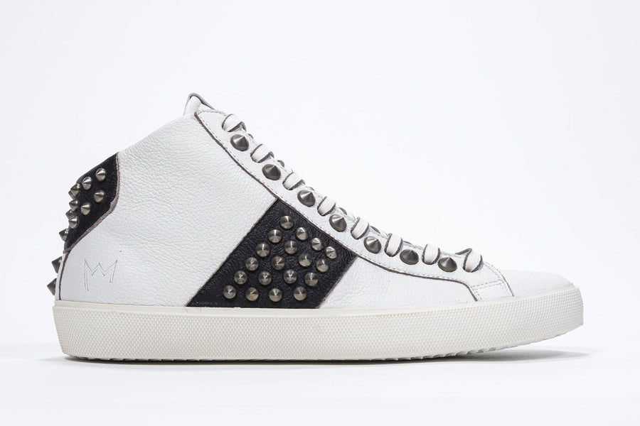 Side profile of mid top white and black sneaker. Full leather upper with studs, an internal zip and vintage rubber sole.
