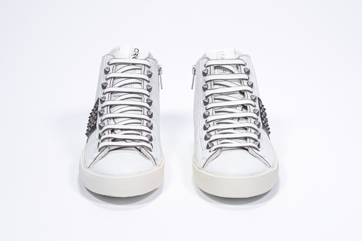 Vue de face d'une paire de chaussures blanches et noires sneaker. Tige en cuir avec clous, fermeture à glissière interne et semelle en caoutchouc vintage.
