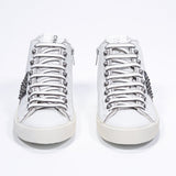 Front view of mid top white and black sneaker. Full leather upper with studs, an internal zip and vintage rubber sole.