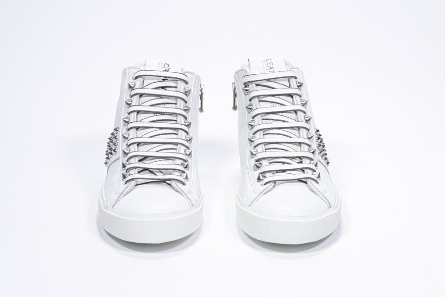 Front view of mid top white sneaker. Full leather upper with studs, an internal zip and white rubber sole.
