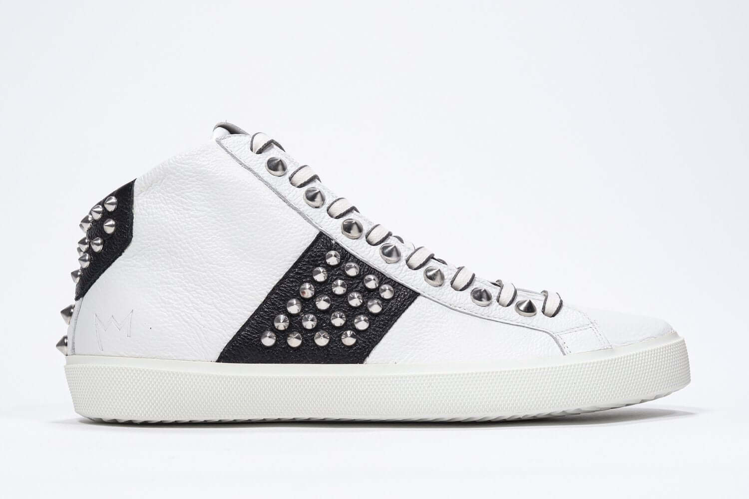 Side profile of mid top white and black sneaker. Full leather upper with studs, an internal zip and white rubber sole.