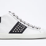Side profile of mid top white and black sneaker. Full leather upper with studs, an internal zip and white rubber sole.