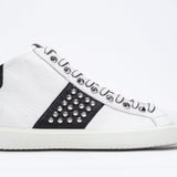 Side profile of mid top white and black sneaker. Full leather upper with studs, an internal zip and white rubber sole.