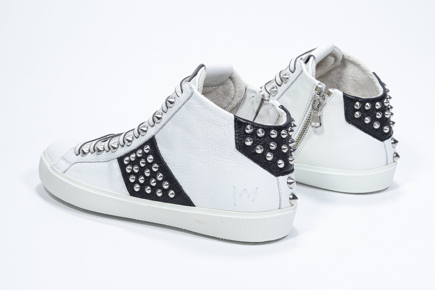 Vue de trois quarts arrière d'un modèle intermédiaire blanc et noir sneaker. Tige en cuir avec clous, fermeture à glissière interne et semelle en caoutchouc blanc.