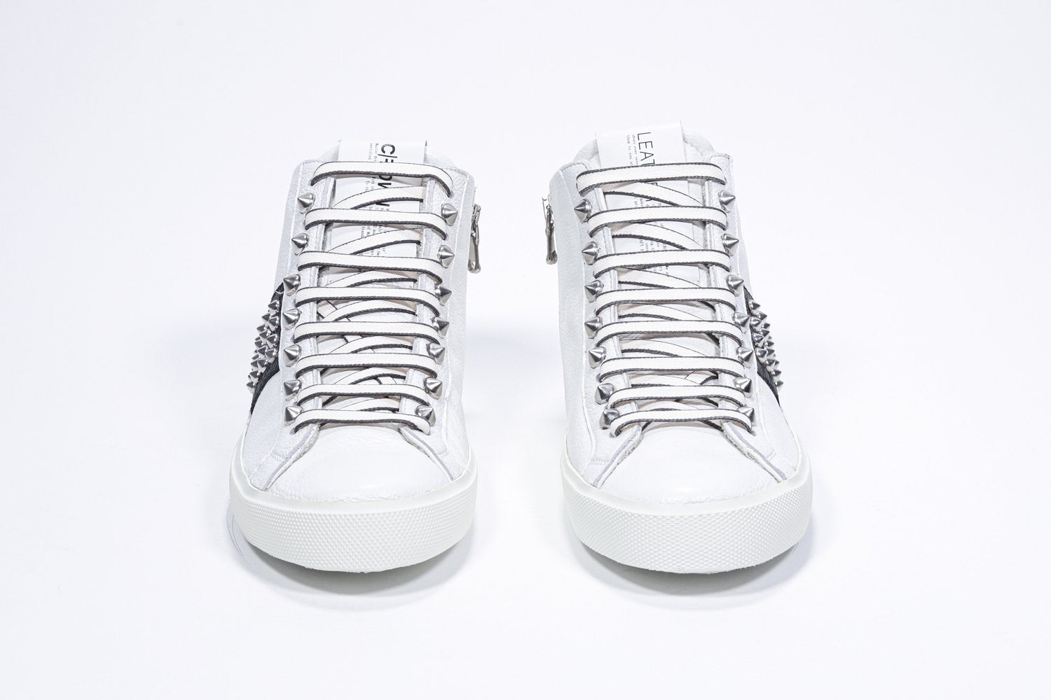 Vista frontale della mid top bianca e nera sneaker. Tomaia in pelle con borchie, zip interna e suola in gomma bianca.