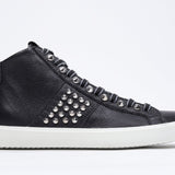 Side profile of mid top black sneaker. Full leather upper with studs, an internal zip and white rubber sole.