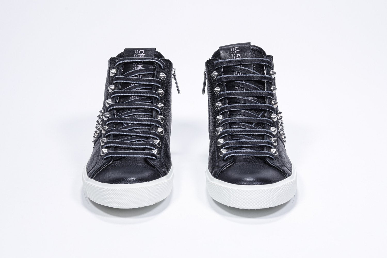 Vue de face de la chaussure de sport noire sneaker. Tige en cuir avec clous, fermeture à glissière intérieure et semelle en caoutchouc blanc.