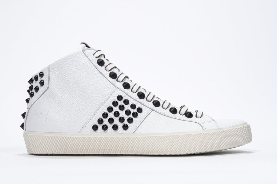 Side profile of mid top white sneaker. Full leather upper with studs, an internal zip and vintage rubber sole.