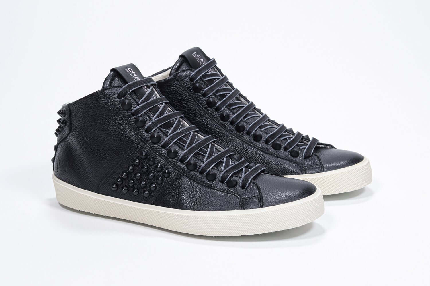 Three quarter front view of mid top black sneaker. Full leather upper with studs, an internal zip and vintage rubber sole.