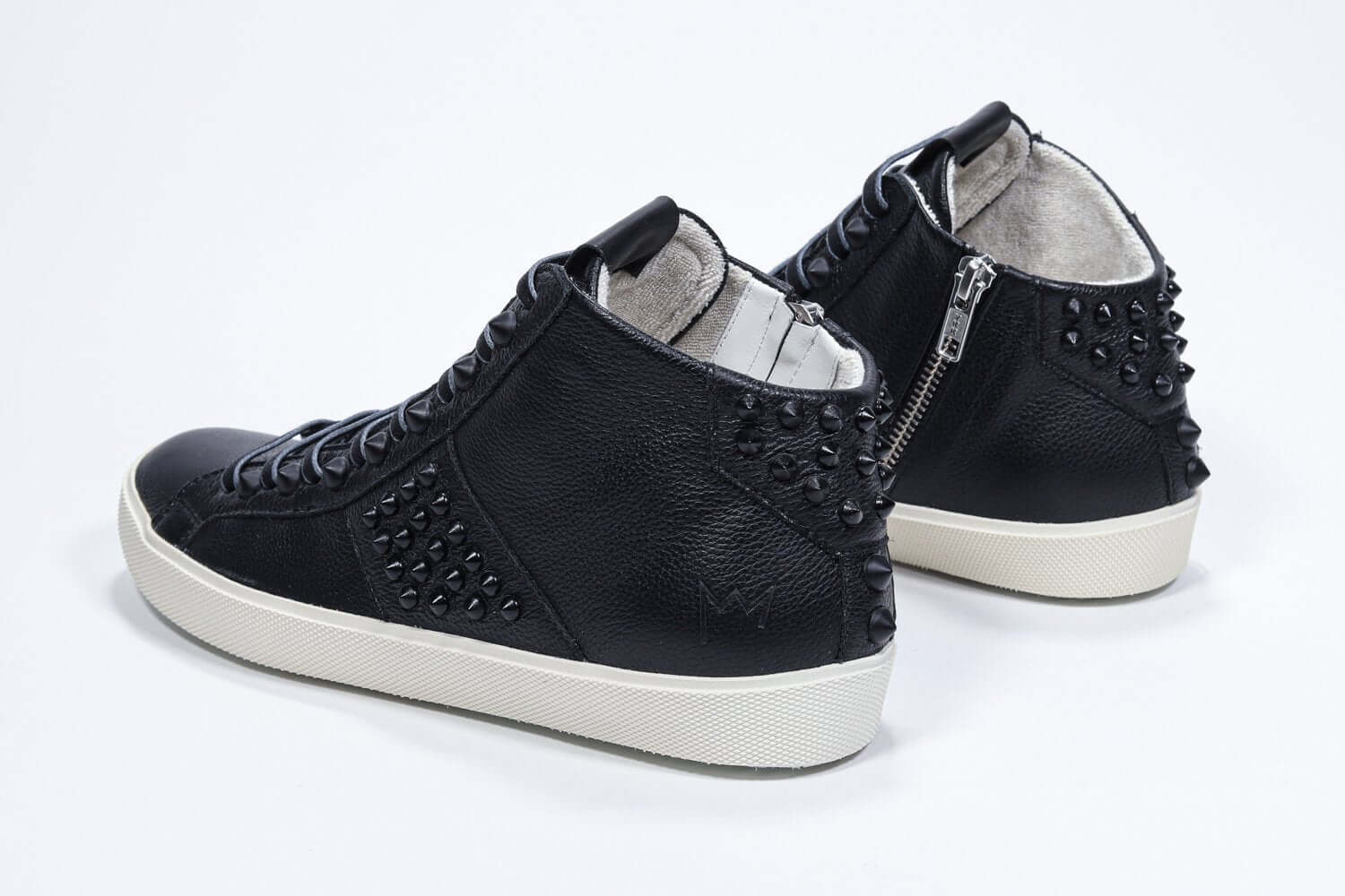Three quarter back view of mid top black sneaker. Full leather upper with studs, an internal zip and vintage rubber sole.