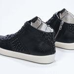 Three quarter back view of mid top black sneaker. Full leather upper with studs, an internal zip and vintage rubber sole.