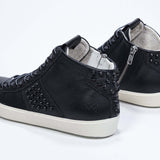 Three quarter back view of mid top black sneaker. Full leather upper with studs, an internal zip and vintage rubber sole.