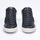 Front view of mid top black sneaker. Full leather upper with studs, an internal zip and vintage rubber sole.