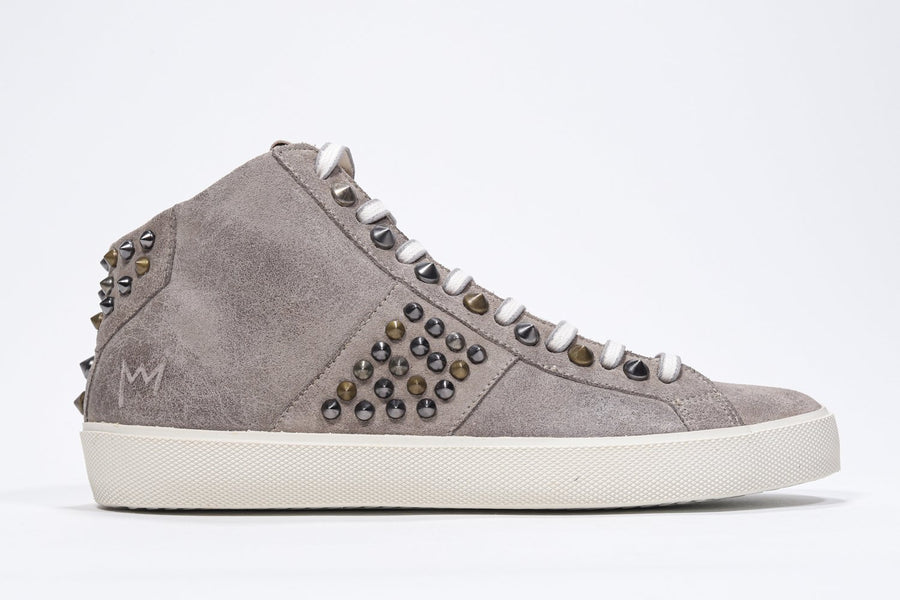 Side profile of mid top beige sneaker. Full suede upper with studs, an internal zip and vintage rubber sole.