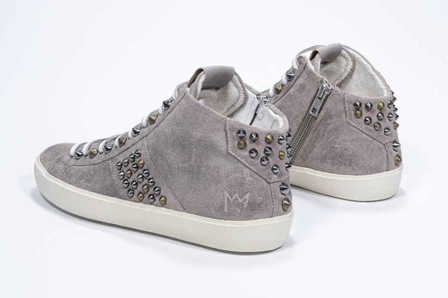 Three quarter back view of mid top beige sneaker. Full suede upper with studs, an internal zip and vintage rubber sole.