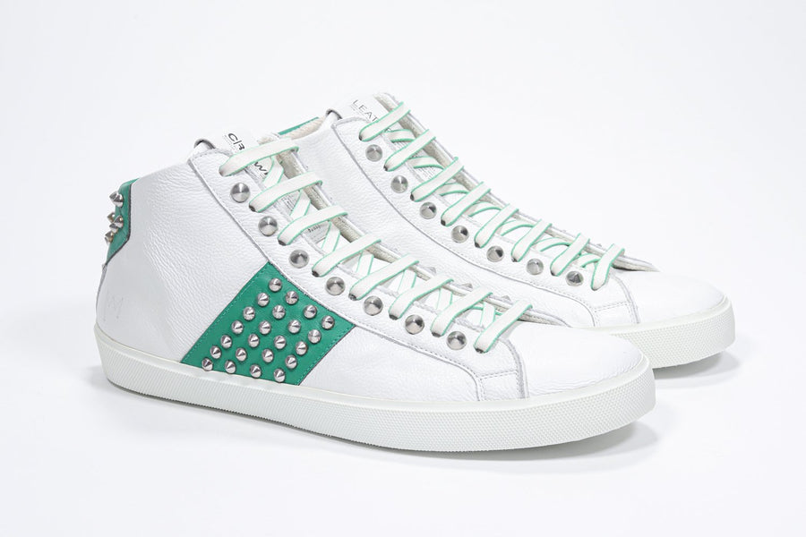 Three quarter front view of mid top white and green sneaker. Full leather upper with studs, an internal zip and white rubber sole.