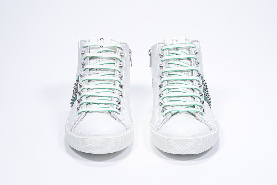 Front view of mid top white and green sneaker. Full leather upper with studs, an internal zip and white rubber sole.