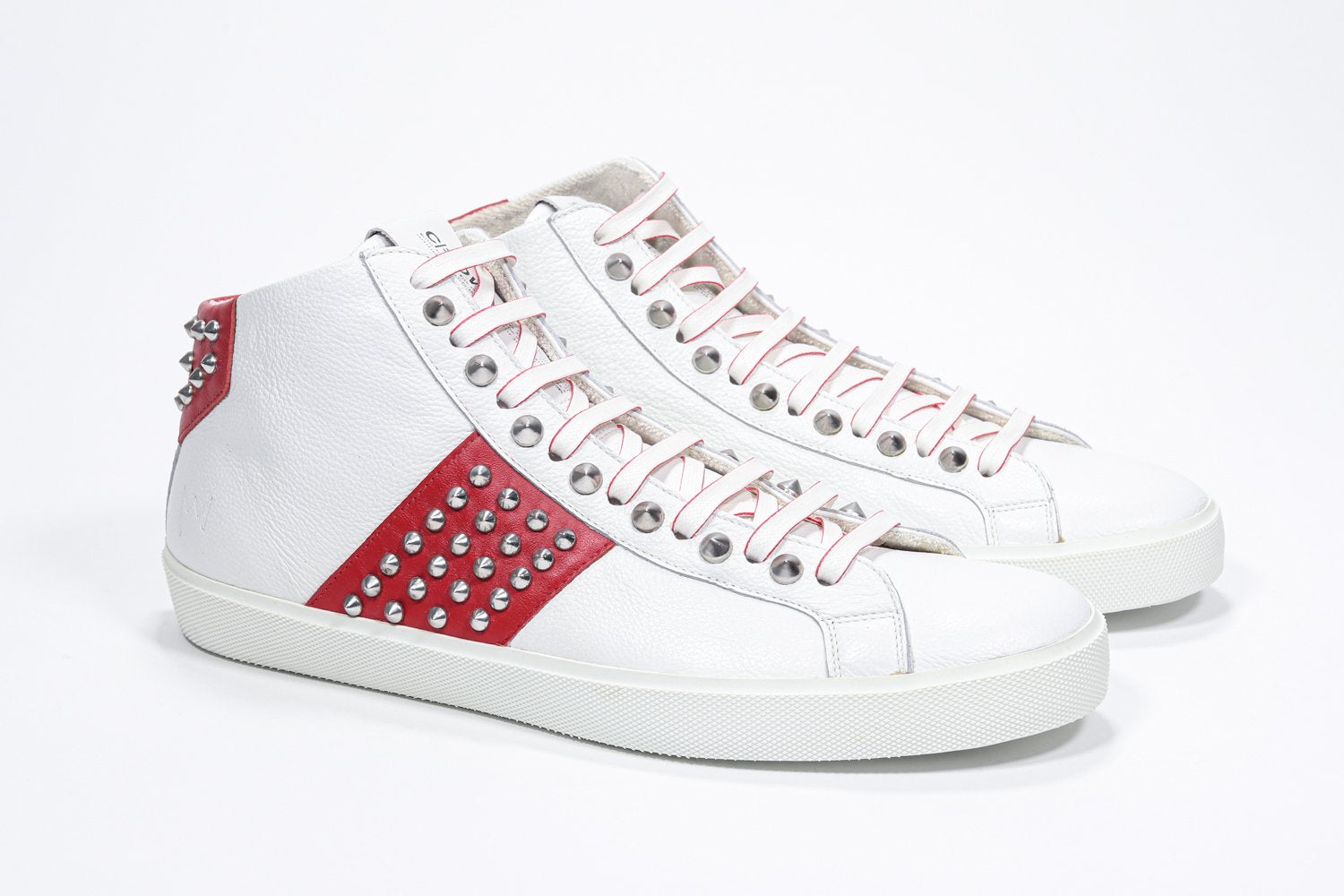 Vue de trois quarts de l'avant d'un top moyen blanc et rouge sneaker. Tige en cuir avec clous, fermeture à glissière interne et semelle en caoutchouc blanc.