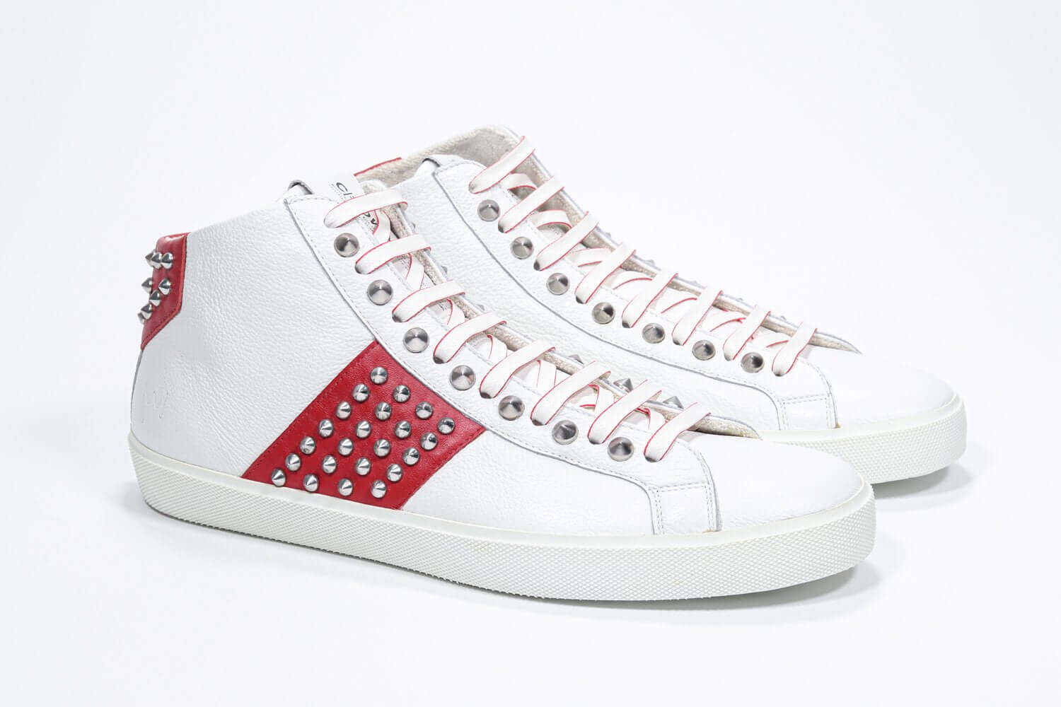 Three quarter front view of mid top white and red sneaker. Full leather upper with studs, an internal zip and white rubber sole.