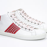 Three quarter front view of mid top white and red sneaker. Full leather upper with studs, an internal zip and white rubber sole.