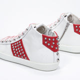 Vista posteriore a tre quarti del mid top bianco e rosso sneaker. Tomaia in pelle con borchie, zip interna e suola in gomma bianca.