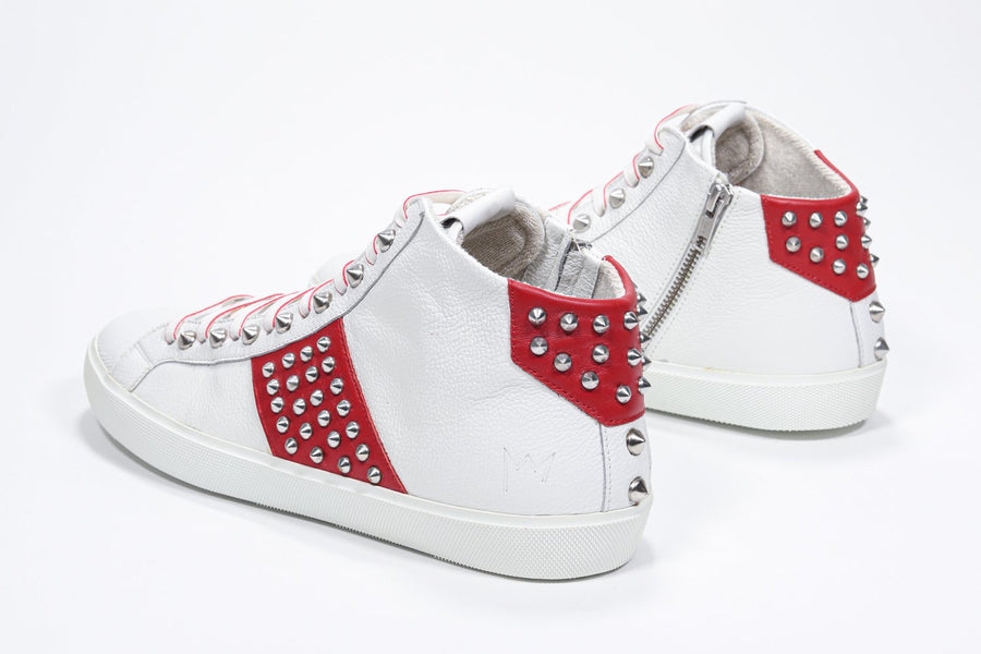 Three quarter back view of mid top white and red sneaker. Full leather upper with studs, an internal zip and white rubber sole.