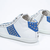 Three quarter back view of mid top white and royal blue sneaker. Full leather upper with studs, an internal zip and white rubber sole.