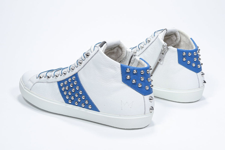 Three quarter back view of mid top white and royal blue sneaker. Full leather upper with studs, an internal zip and white rubber sole.