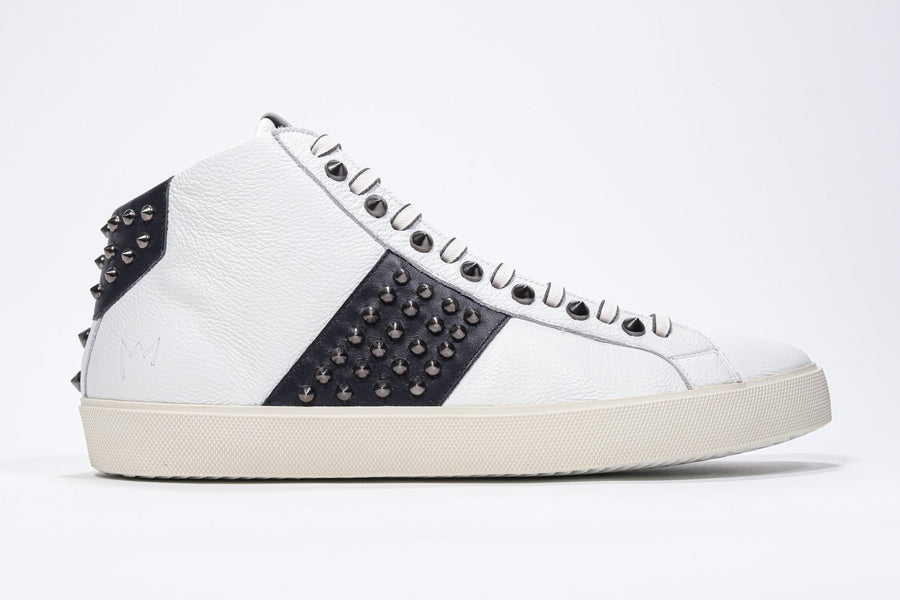 Side profile of mid top white and navy sneaker. Full leather upper with studs, an internal zip and vintage rubber sole.