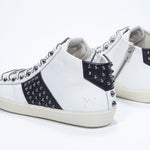 Three quarter back view of mid top white and navy sneaker. Full leather upper with studs, an internal zip and vintage rubber sole.