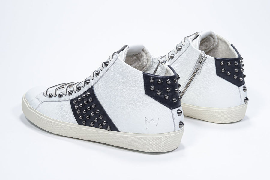Three quarter back view of mid top white and navy sneaker. Full leather upper with studs, an internal zip and vintage rubber sole.