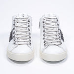 Front view of mid top white and navy sneaker. Full leather upper with studs, an internal zip and vintage rubber sole.