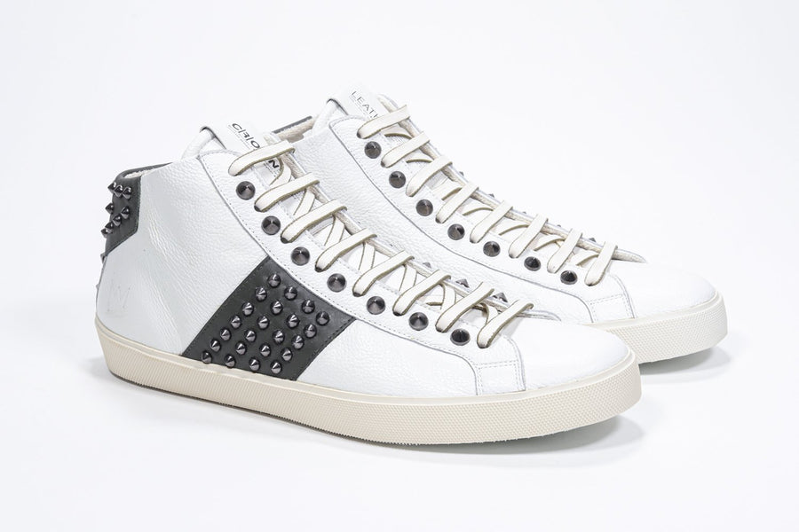 Three quarter front view of mid top white and military green sneaker. Full leather upper with studs, an internal zip and vintage rubber sole.