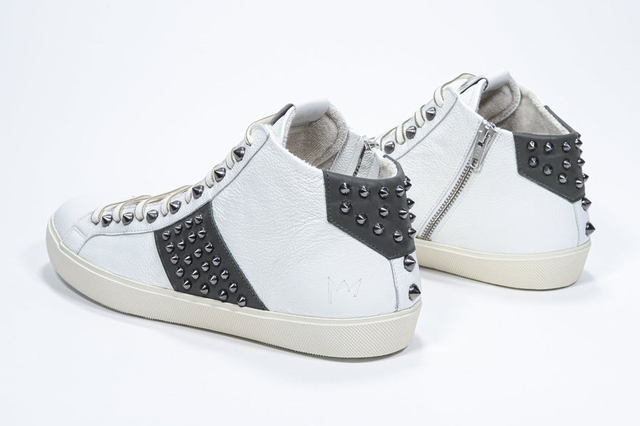 Three quarter back view of mid top white and military green sneaker. Full leather upper with studs, an internal zip and vintage rubber sole.
