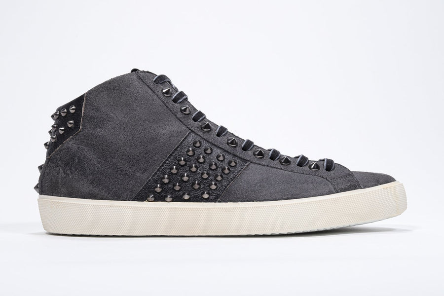 Side profile of mid top dark grey sneaker. Suede and leather upper with studs, an internal zip and vintage rubber sole.