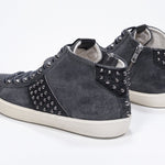 Three quarter back view of mid top dark grey sneaker. Suede and leather upper with studs, an internal zip and vintage rubber sole.